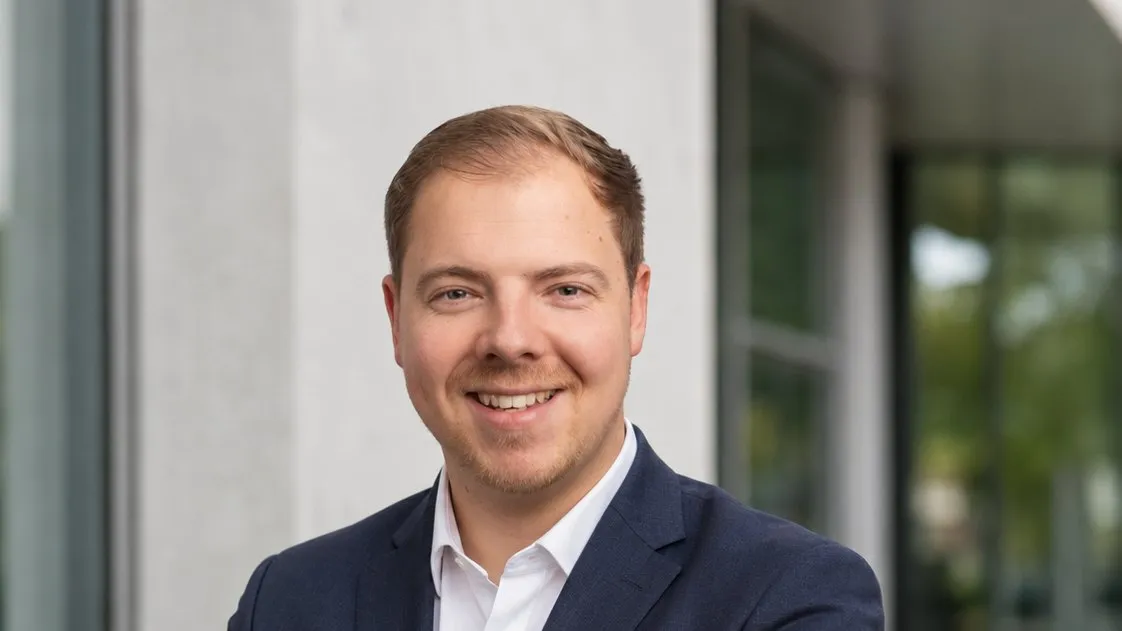 Jan Achnitz im dunkelblauen Anzug vor einem modernen Bürogebäude
